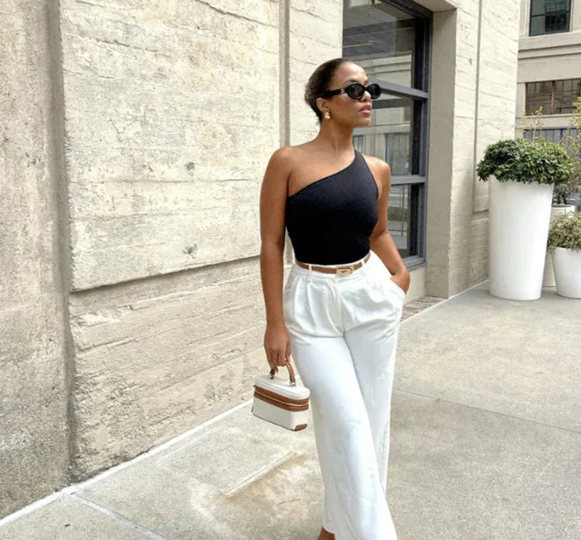 Woman in stylish outfit with black one-shoulder top and white pants, walking outdoors.